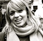 A black and white photograph of Enrica Fei, smiling wide, her light hair waving over her thick scarf and dark top.
